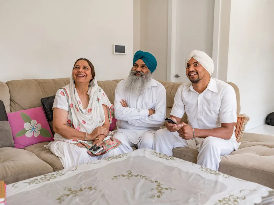 An older couple and their adult son sit smiling together on a sofa at home