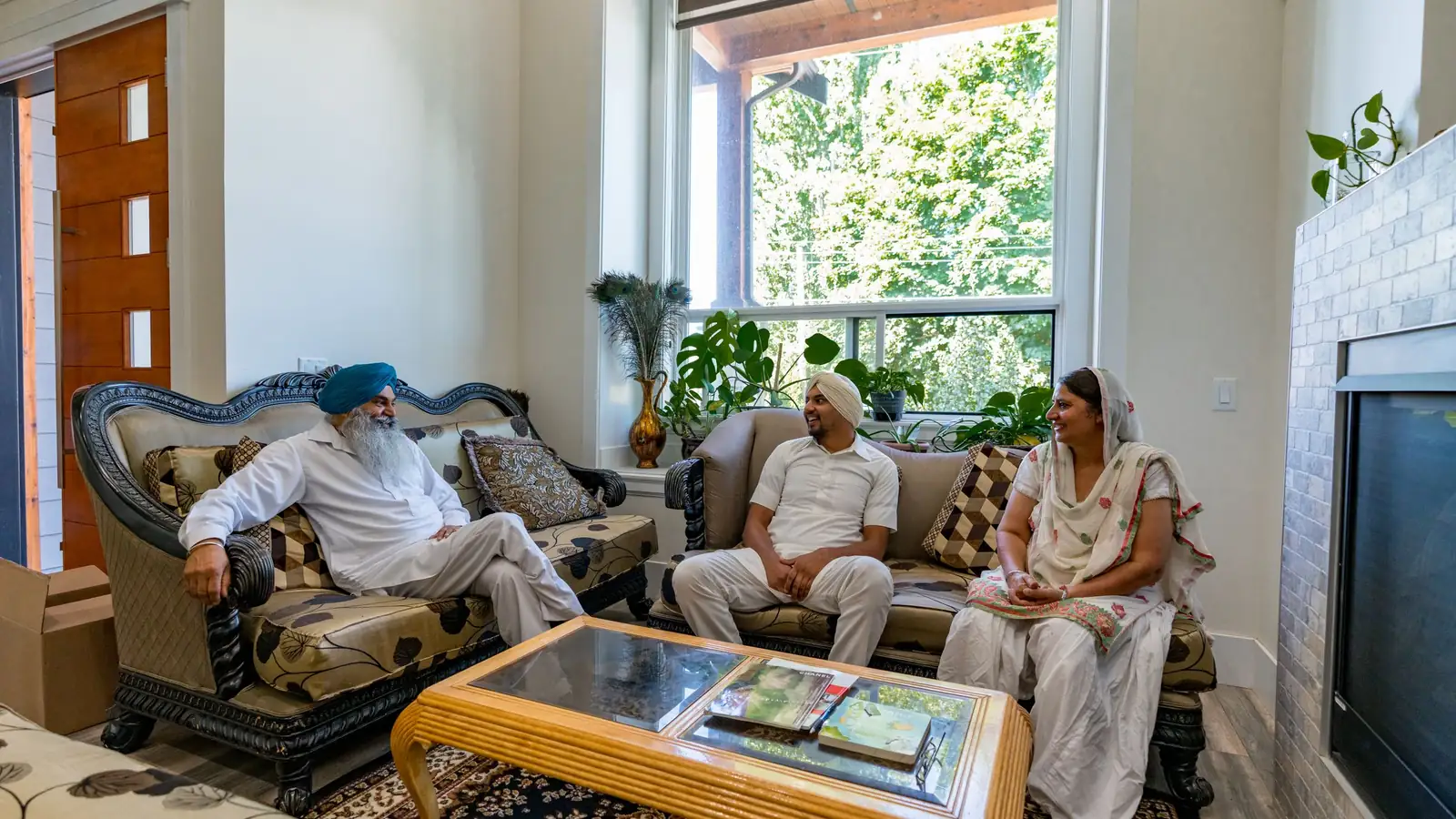 An older couple and a younger man talk in a bright living room