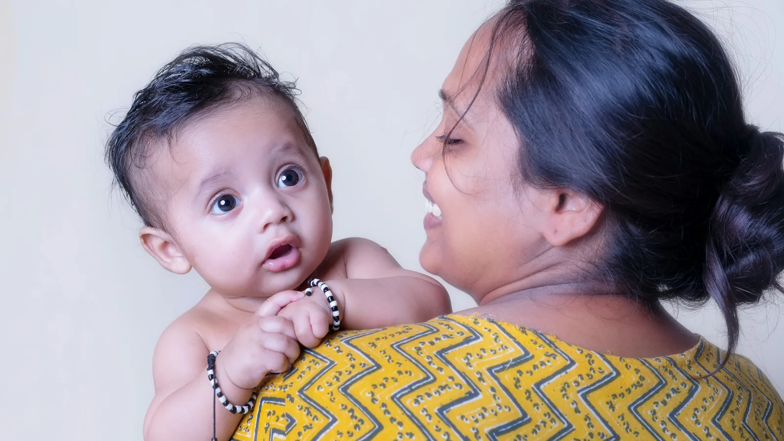 A smiling mother holds her baby over her shoulder