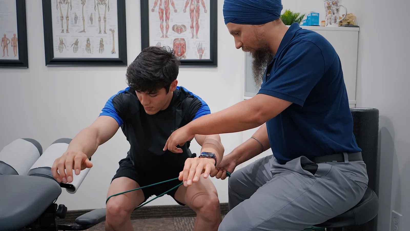 A physiotherapist guides a young man through a resistance band arm exercise